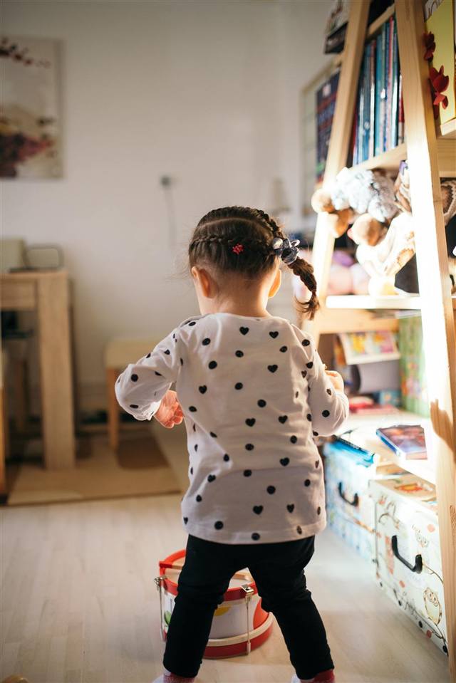Criança brincando entre livros e brinquedos em um quarto aconchegante
